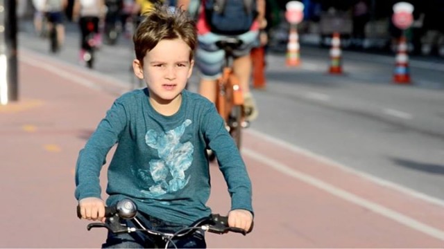 Criança pedalando em ciclovia, sem capacete.