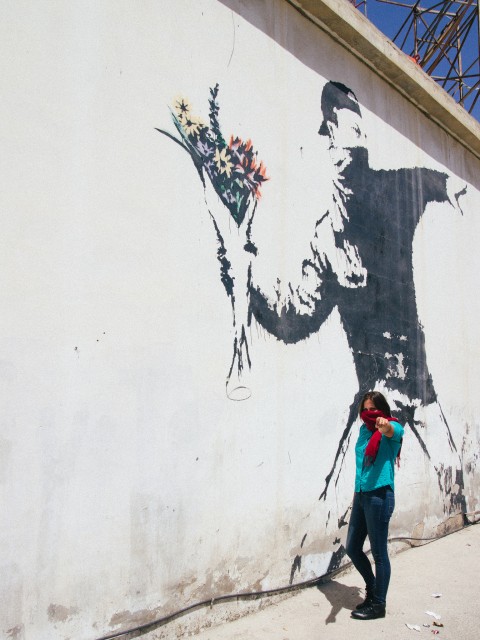 Talita e o grafite do famoso Banksy, que tem um manifestante de máscara atirando um buque de flores em vez de um coquetel molotov