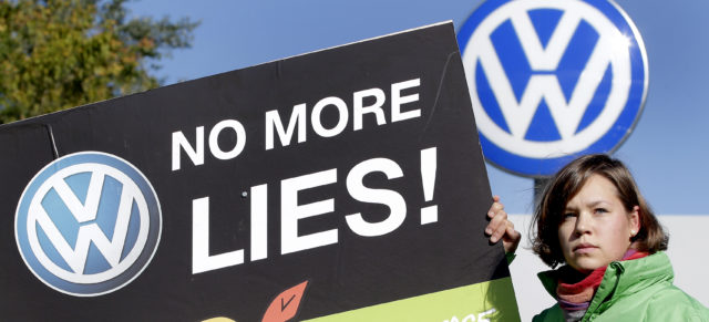 An activist of the environmental protection organization 'Greenpeace' holds a protest poster in front of a factory gate of the German car manufacturer Volkswagen in Wolfsburg, Germany, Friday, Sept. 25, 2015. (AP Photo/Michael Sohn)