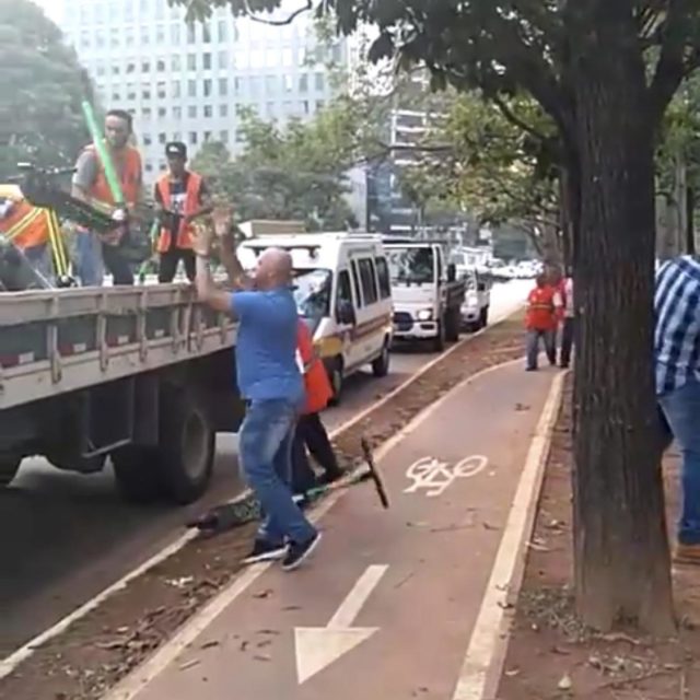 Homem a serviço da Prefeitura de São Paulo recolhe patinetes elétricos estacionados próximos à ciclovia da Av. Faria Lima e os joga na carroceria de um caminhão.